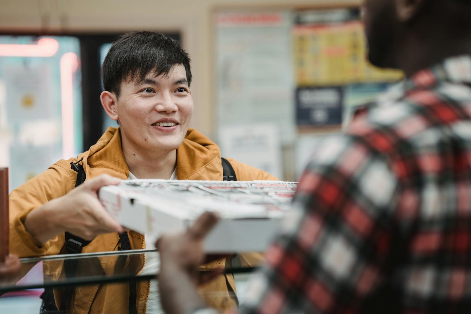 Man in a Yellow Jacket Buying a Box of Pizza